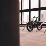 A modern electric bicycle parked indoors near a large glass wall with steel racks.