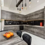 Table with bouquet and fruits placed near gray cupboards and modern kitchenware in spacious kitchen with lamps and creative design
