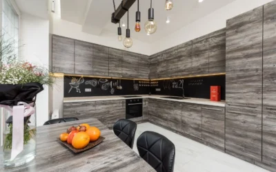 Table with bouquet and fruits placed near gray cupboards and modern kitchenware in spacious kitchen with lamps and creative design