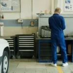 Mechanic in blue overalls inspecting a white car in a well-equipped garage.
