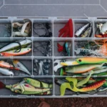 A top view of a tackle box filled with various colorful fishing lures and equipment.