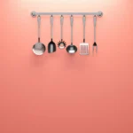 Hanging kitchen utensils against a coral backdrop, ideal for minimalistic design concepts.