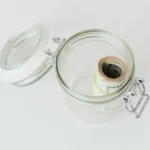 Close-up shot of rolled US dollar bills inside a glass jar on a white surface.