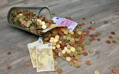 A glass jar with euro coins and banknotes spilled on a wooden surface, representing finance and savings.