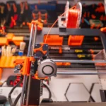 Detailed view of a 3D printer with filament and tools in a workshop setting.