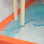 High angle of timber object placed above transparent glass with colored water as art installation