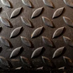 Close-up of a diamond plate metal surface with an oblique textured pattern.