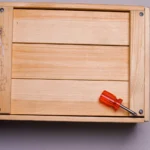 A wooden box with a red screwdriver lying on a flat surface, ideal for tool and carpentry themes.