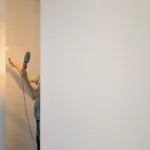 Crop faceless male holding lamp and paint roller while renovating walls at home