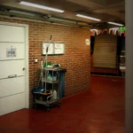 A brightly lit industrial hallway with a cleaning cart and supplies near an office door.