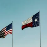 American and Texas flags waving under a clear blue sky, symbolizing patriotism and freedom.