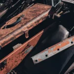 A vintage rusty toolbox amidst scrap metal pieces in a junkyard under sunlight.