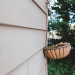 Round shaped pot with small green plant hanging on chain on building wall in garden