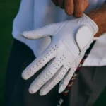 Close-up of a golfer adjusting their white glove with a club, outdoors.