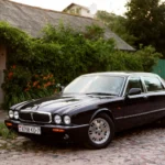 Classic Jaguar XJ car parked in a serene outdoor setting with lush greenery.