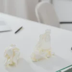 A clean white workspace featuring a laptop, phone, and crumpled papers.