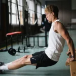 Side view of muscular sportsman in sportswear and glasses doing tricep dips exercises in gym