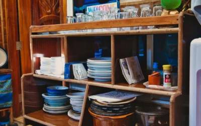 A wooden kitchen shelf stocked with assorted dishes, glasses, and condiments. Cozy vintage style.