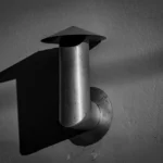 Black and white image of a metal pipe creating a striking shadow on a wall.