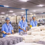 Three female workers in blue uniforms rolling towels in a textile factory.