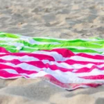 Bright green and pink striped beach towels laying on a sandy beach, symbolizing relaxation and summer vibes.