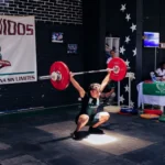 Athlete executing a snatch lift at a weightlifting competition indoors.
