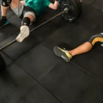 Athletes resting on a gym floor beside heavy barbells after an intense weightlifting session.