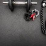 Flat lay of gym equipment including a dumbbell, weights, and rope on a dark surface ideal for fitness themes.