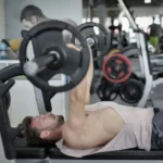 Side view of strong young sportsman in sportswear lying on bench and pressing heavy barbell doing chest exercise training in modern gym