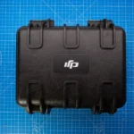 A black protective hard case on a blue grid background, ideal for travel and equipment storage.