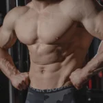 Detailed image of a muscular male torso flexing in a gym setting, emphasizing strength.